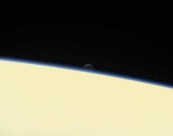 A photo of Enceladus setting behind the planet Saturn.
