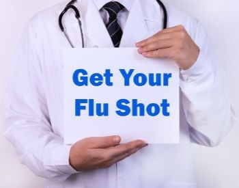A picture of a doctor holding a get your flu shot sign